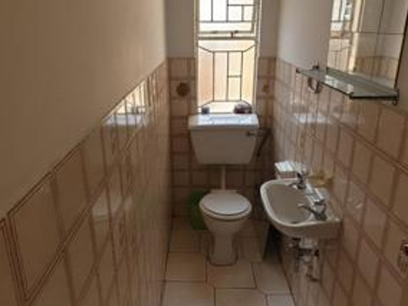 A compact, functional bathroom featuring a toilet, wall-mounted basin, and tiled finishes throughout, providing a basic utility space.