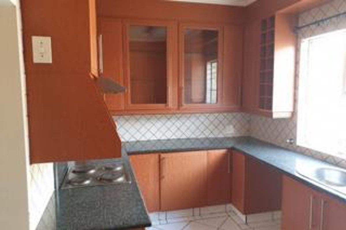 A functional kitchen featuring wooden cabinetry, granite countertops, a built-in electric hob with extractor fan, and a stainless steel sink.