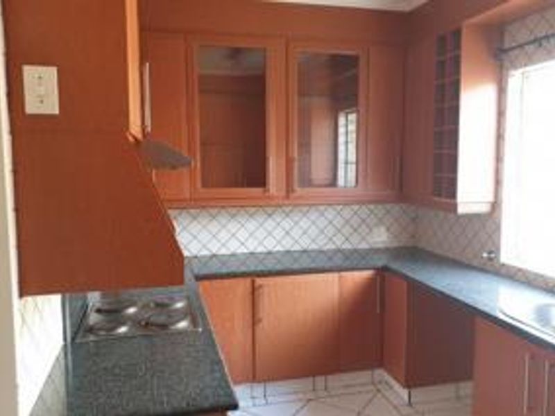 A functional kitchen featuring wooden cabinetry, granite countertops, a built-in electric hob with extractor fan, and a stainless steel sink.