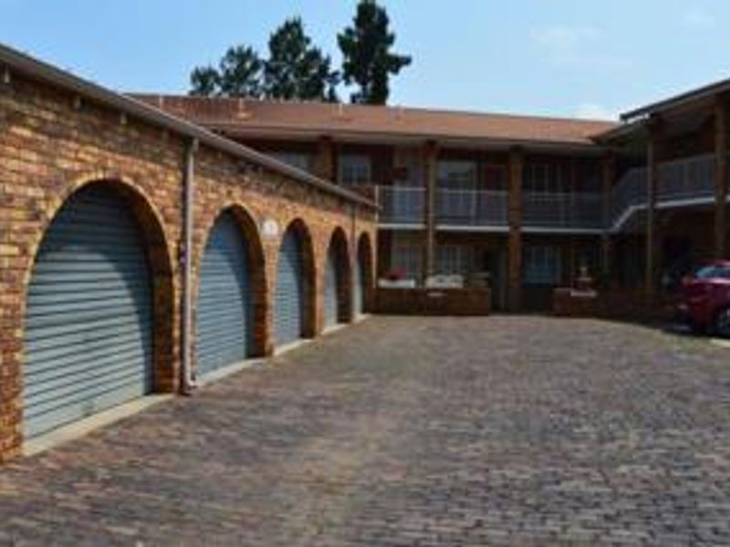 Exterior view of a townhouse complex featuring a paved driveway, multiple arched garage bays with roller shutter doors, and upper-level balcony access.
