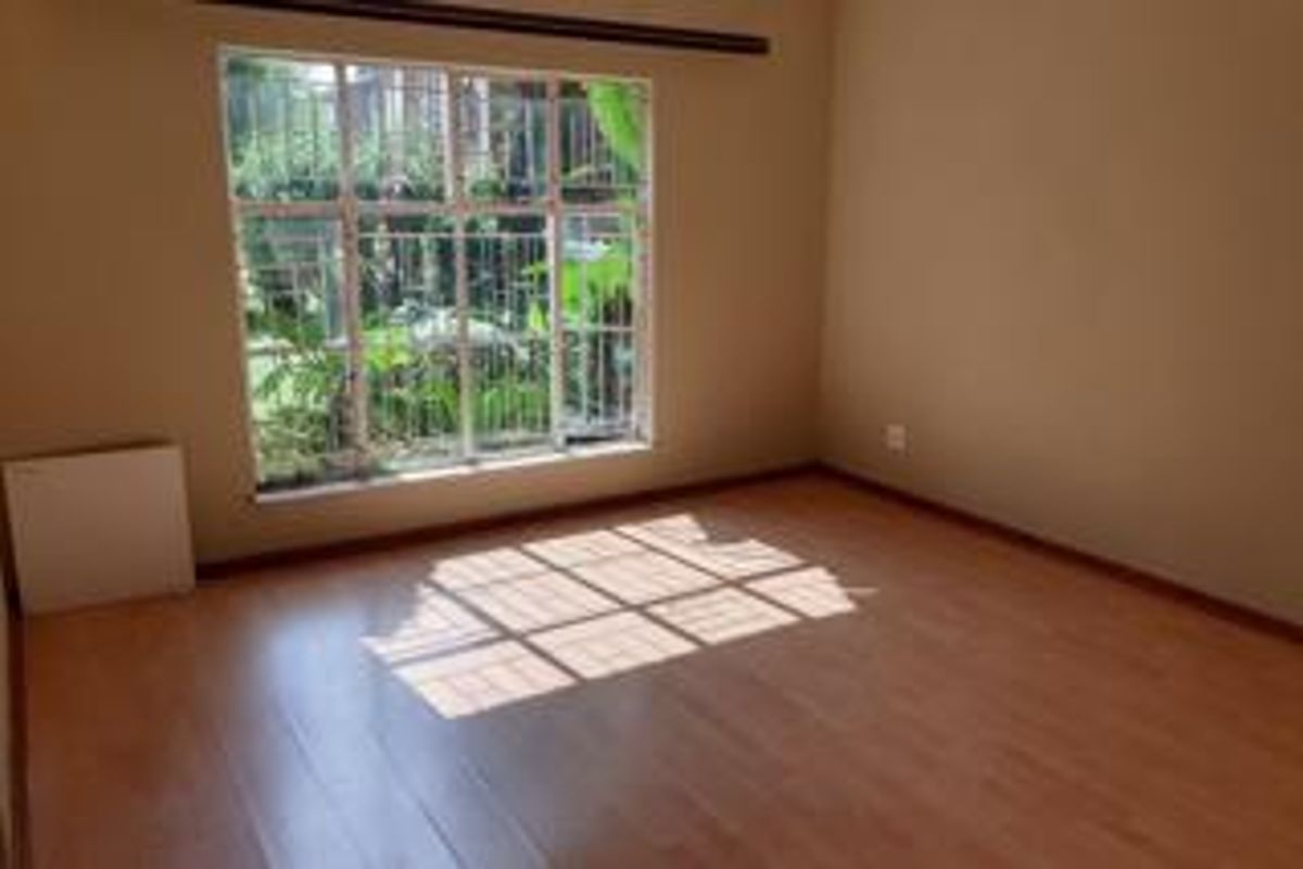 A bright, empty bedroom featuring laminate flooring and a large window with security bars, offering a clean canvas for personalization.