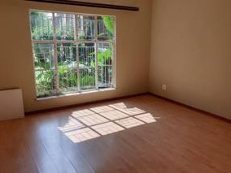 A bright, empty bedroom featuring laminate flooring and a large window with security bars, offering a clean canvas for personalization.