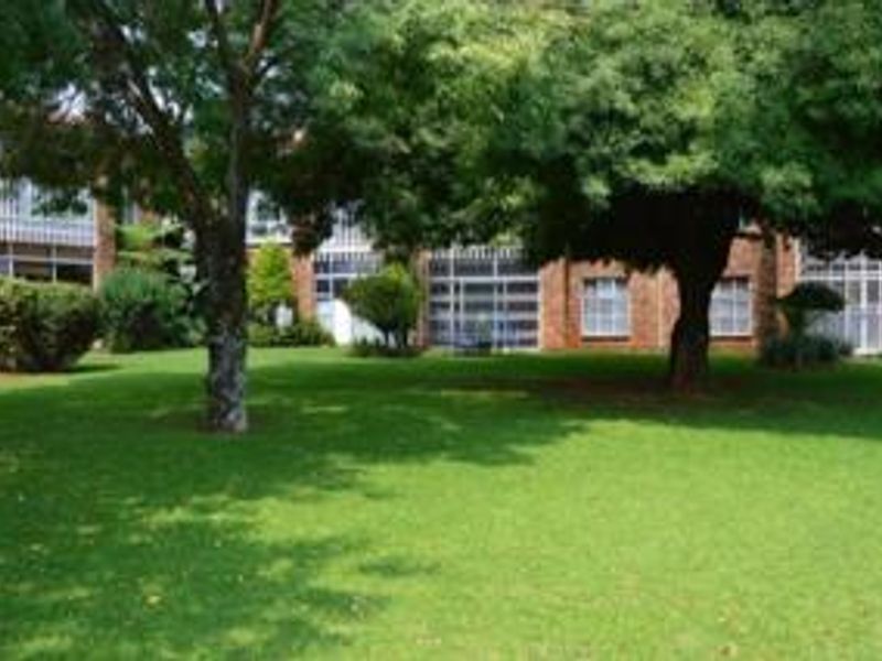 A view of the rear exterior of the townhouse complex, featuring a well-maintained lawn, mature trees, and brick facade with large windows.