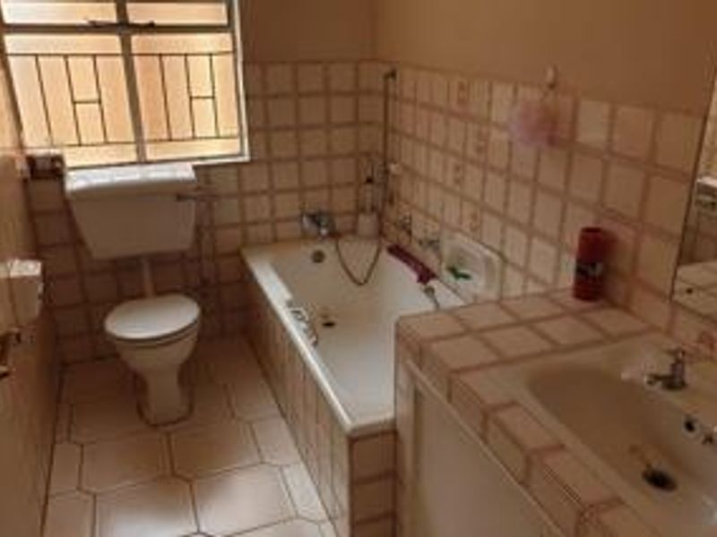 A functional bathroom featuring a built-in bathtub, vanity basin, and toilet, finished with dated ceramic wall and floor tiles.