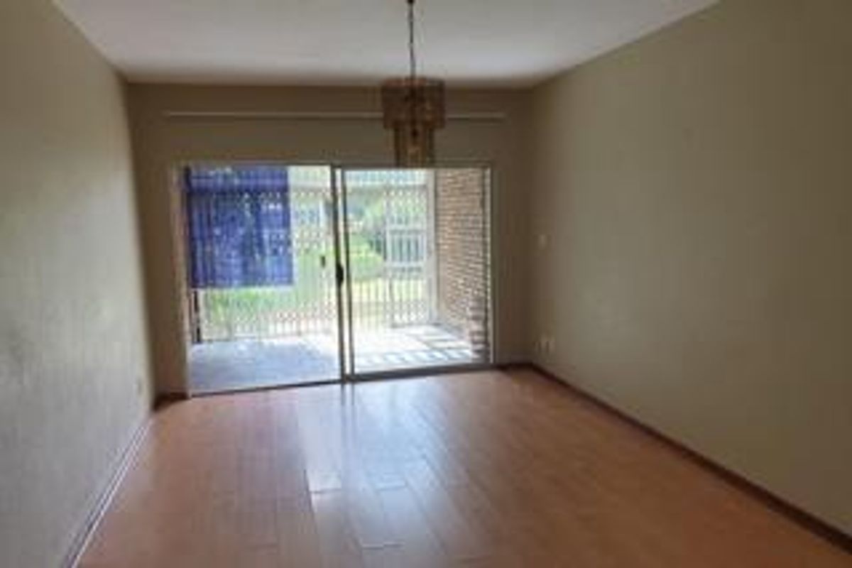An empty living room featuring laminate flooring and a sliding glass door that opens to an outdoor patio area.
