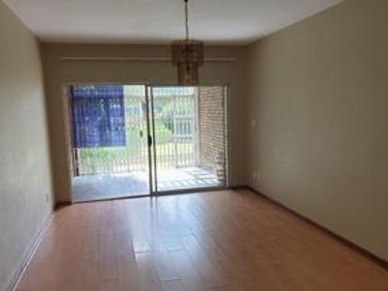 An empty living room featuring laminate flooring and a sliding glass door that opens to an outdoor patio area.