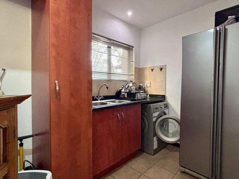 A functional laundry area featuring built-in cabinetry, a stainless steel sink, tiled splashback, and tiled flooring.