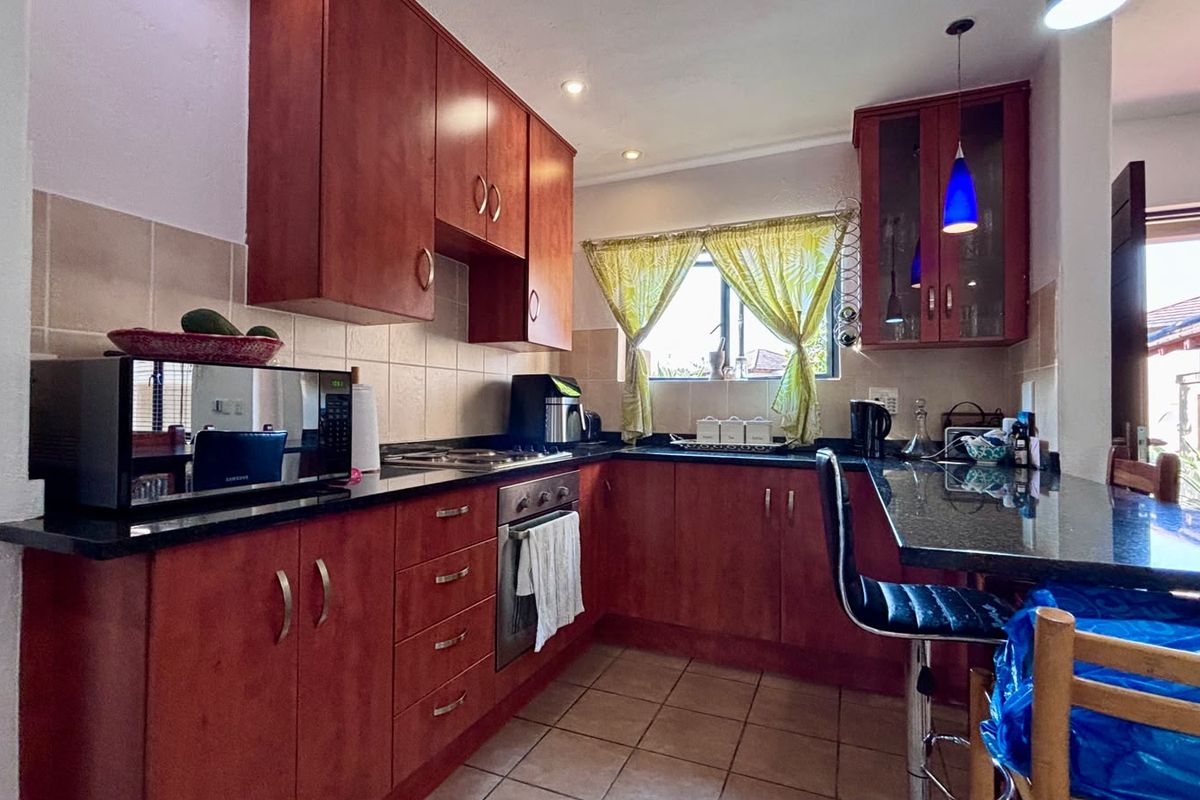 A functional kitchen featuring cherry-wood cabinetry, granite countertops, built-in oven and hob, and tiled flooring with a breakfast bar area.