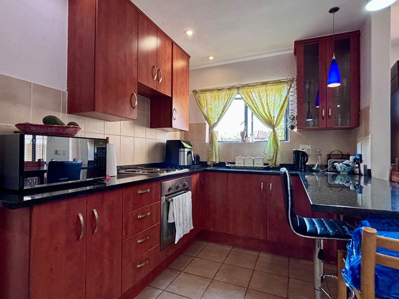 A functional kitchen featuring cherry-wood cabinetry, granite countertops, built-in oven and hob, and tiled flooring with a breakfast bar area.
