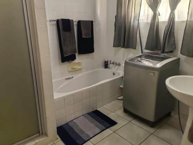 A functional bathroom featuring a built-in bathtub, shower enclosure, and pedestal basin with tiled finishes throughout.