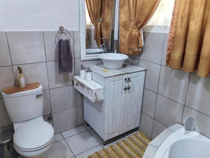 A functional bathroom featuring a vessel sink vanity, wall-mounted mirror, and neutral ceramic tiling throughout.
