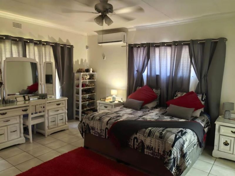 A spacious bedroom featuring tiled flooring, a ceiling fan, and a wall-mounted split-system air conditioner for climate control.