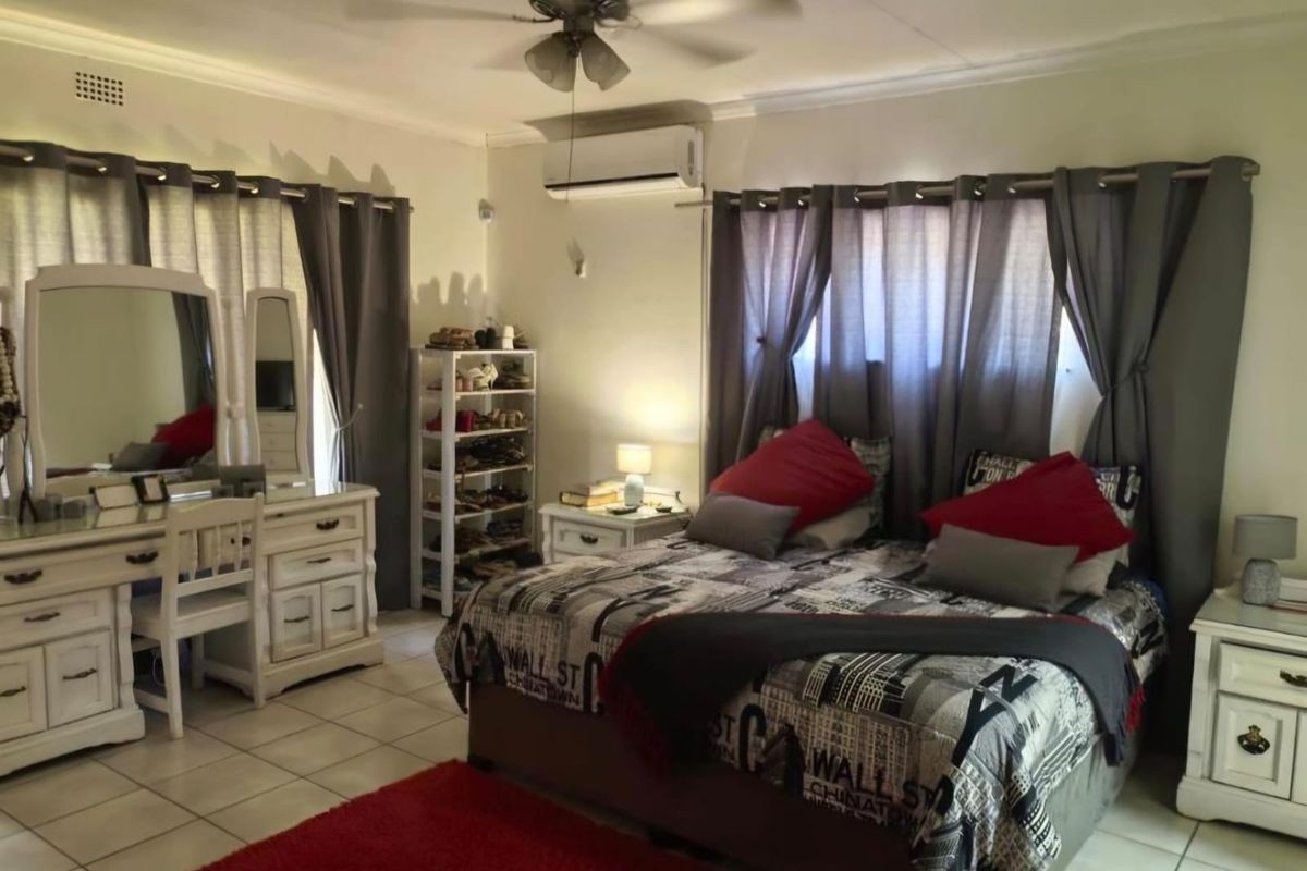 A spacious bedroom featuring tiled flooring, a ceiling fan, and a wall-mounted split-system air conditioner for climate control.