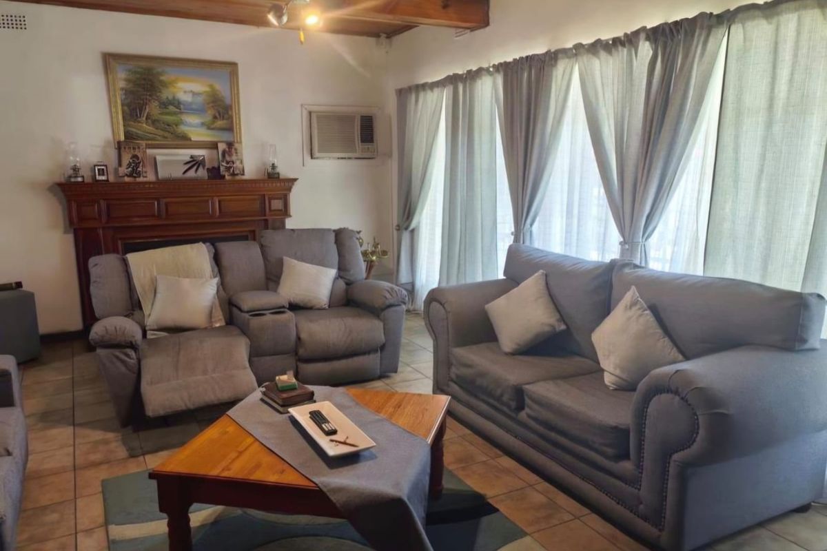 A comfortable living room featuring a fireplace with a wooden mantel, exposed timber ceiling beams, and tiled flooring.