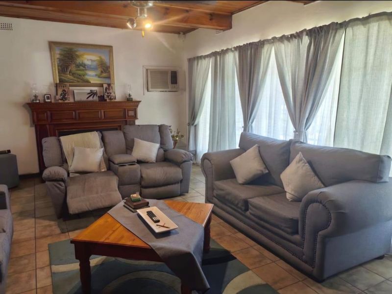 A comfortable living room featuring a fireplace with a wooden mantel, exposed timber ceiling beams, and tiled flooring.