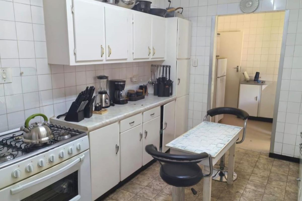 A functional kitchen featuring white cabinetry, a gas stove, and tiled wall finishes, with an adjacent scullery area visible through the doorway.
