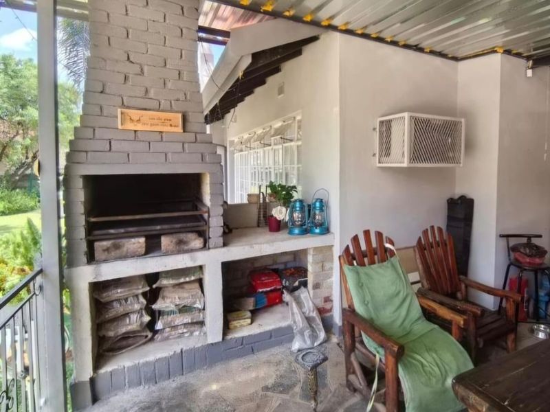 Covered outdoor patio featuring a built-in brick braai, stone flooring, and a corrugated metal roof, providing a functional space for outdoor entertaining.