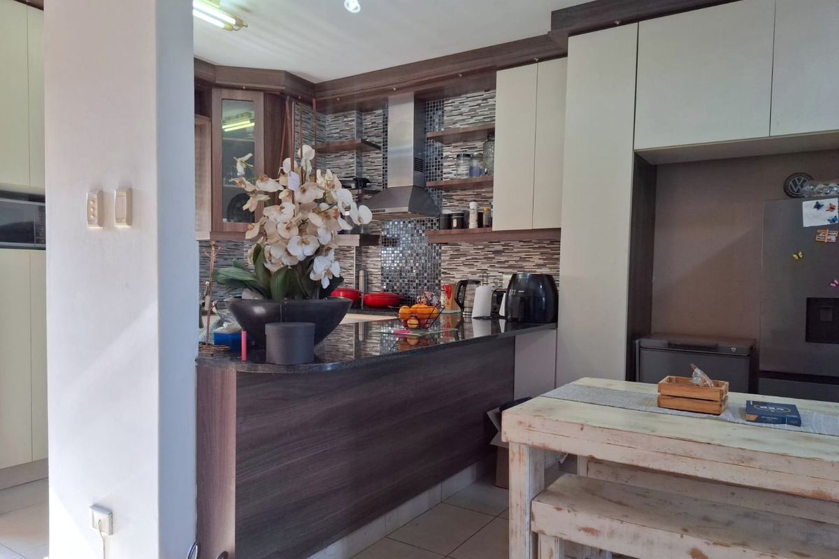 A functional kitchen featuring granite countertops, modern laminate cabinetry, a mosaic tile backsplash, and a stainless steel extractor fan.