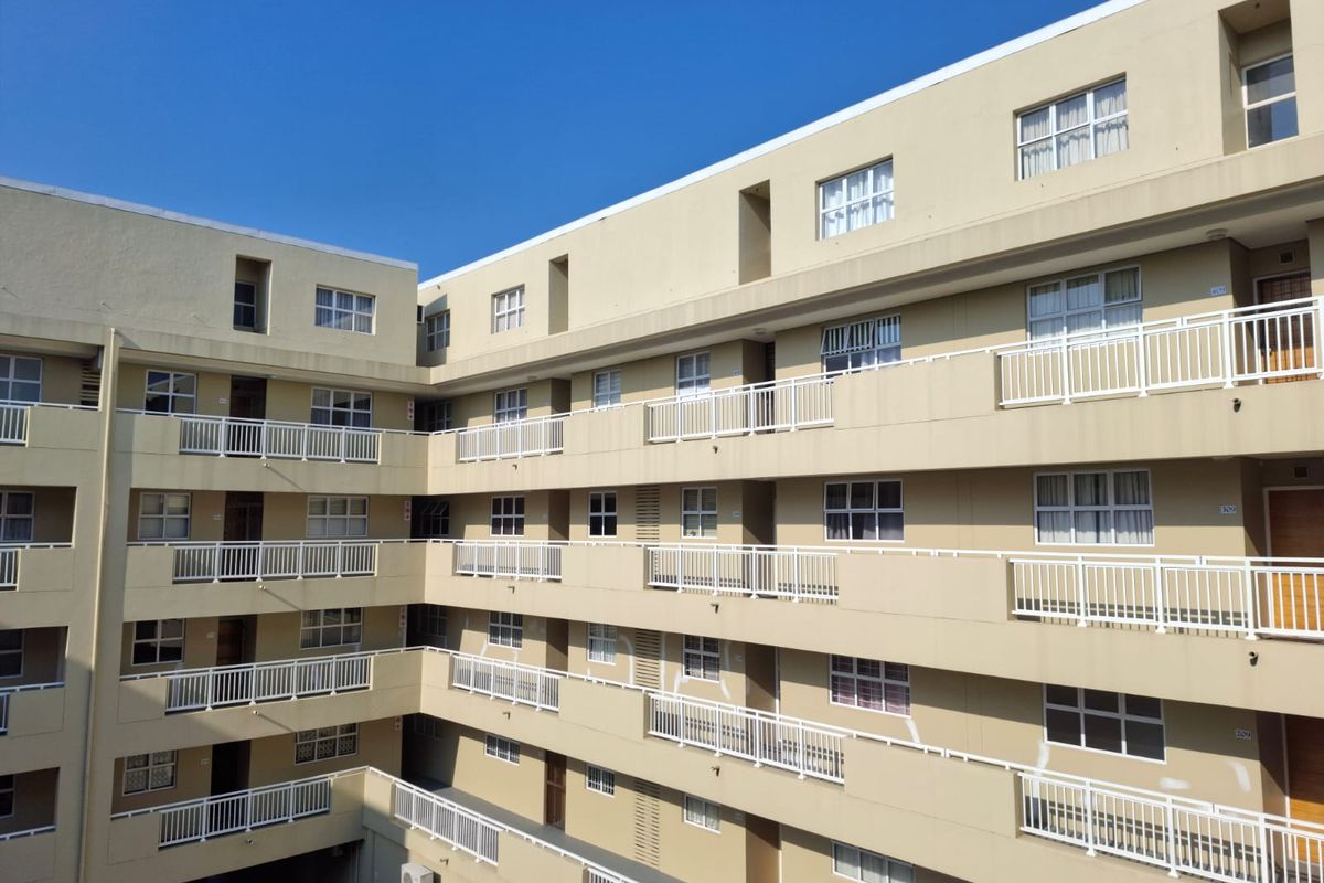 Exterior view of a multi-story apartment building featuring multiple levels of balconies with white railings and uniform window placement.