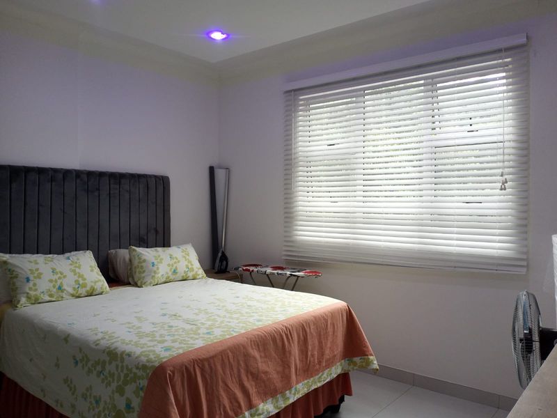 A well-lit bedroom featuring tiled flooring, recessed ceiling lights, and venetian blinds covering the window.