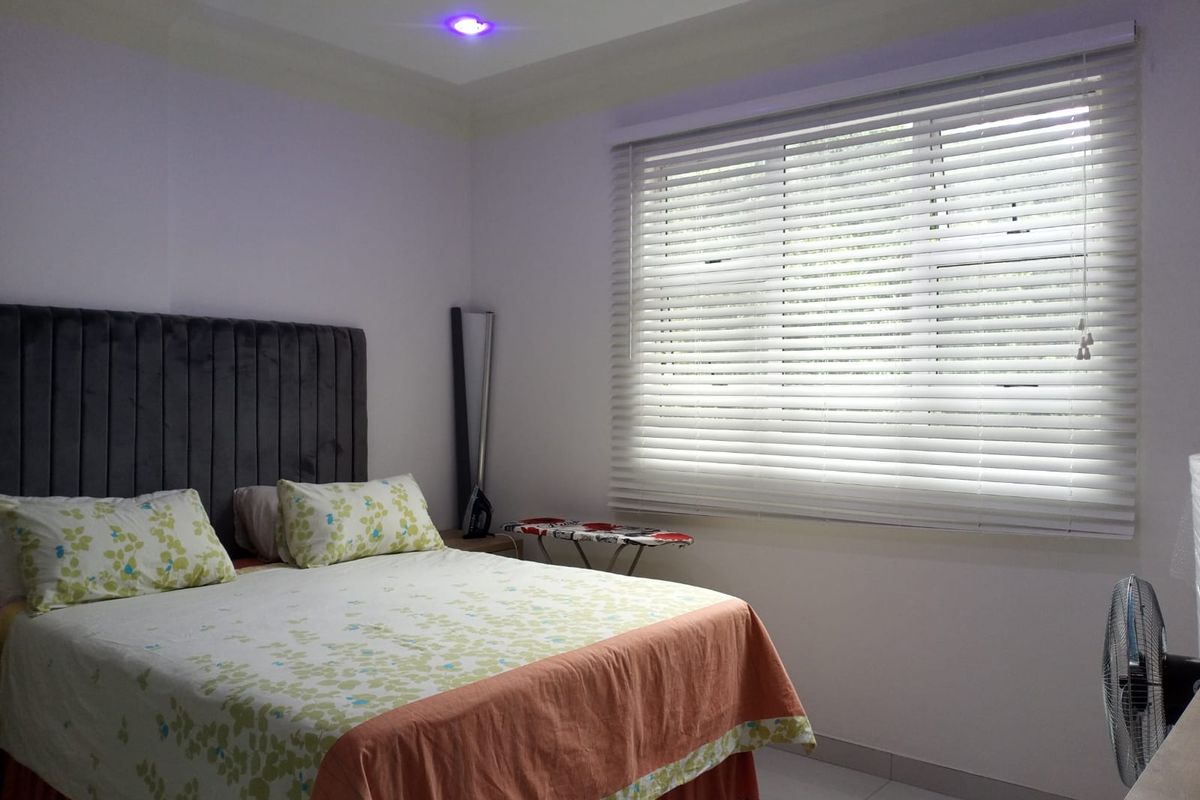 A well-lit bedroom featuring tiled flooring, recessed ceiling lights, and venetian blinds covering the window.