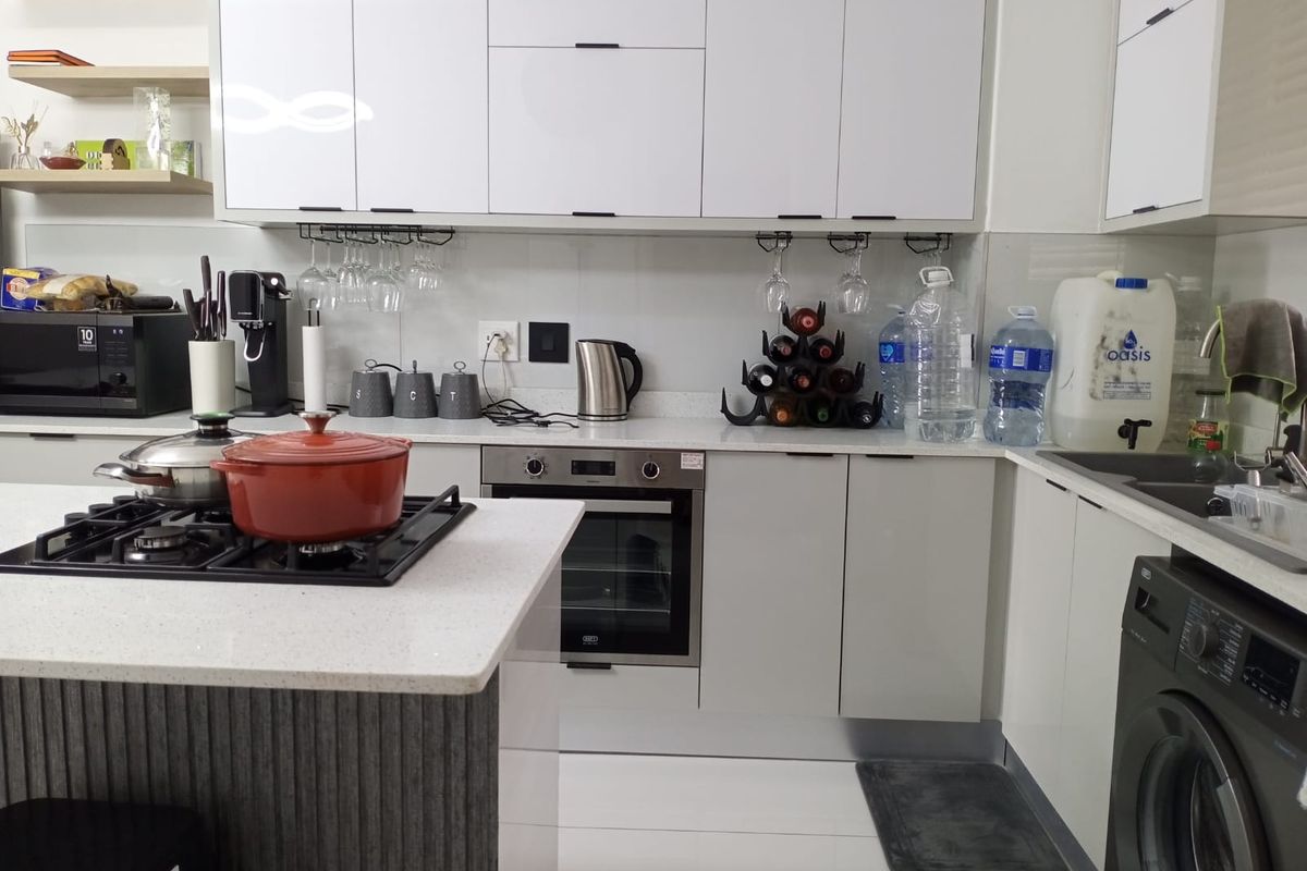 Modern kitchen featuring white cabinetry, stone countertops, a central island with a gas hob, built-in oven, and floating shelving.