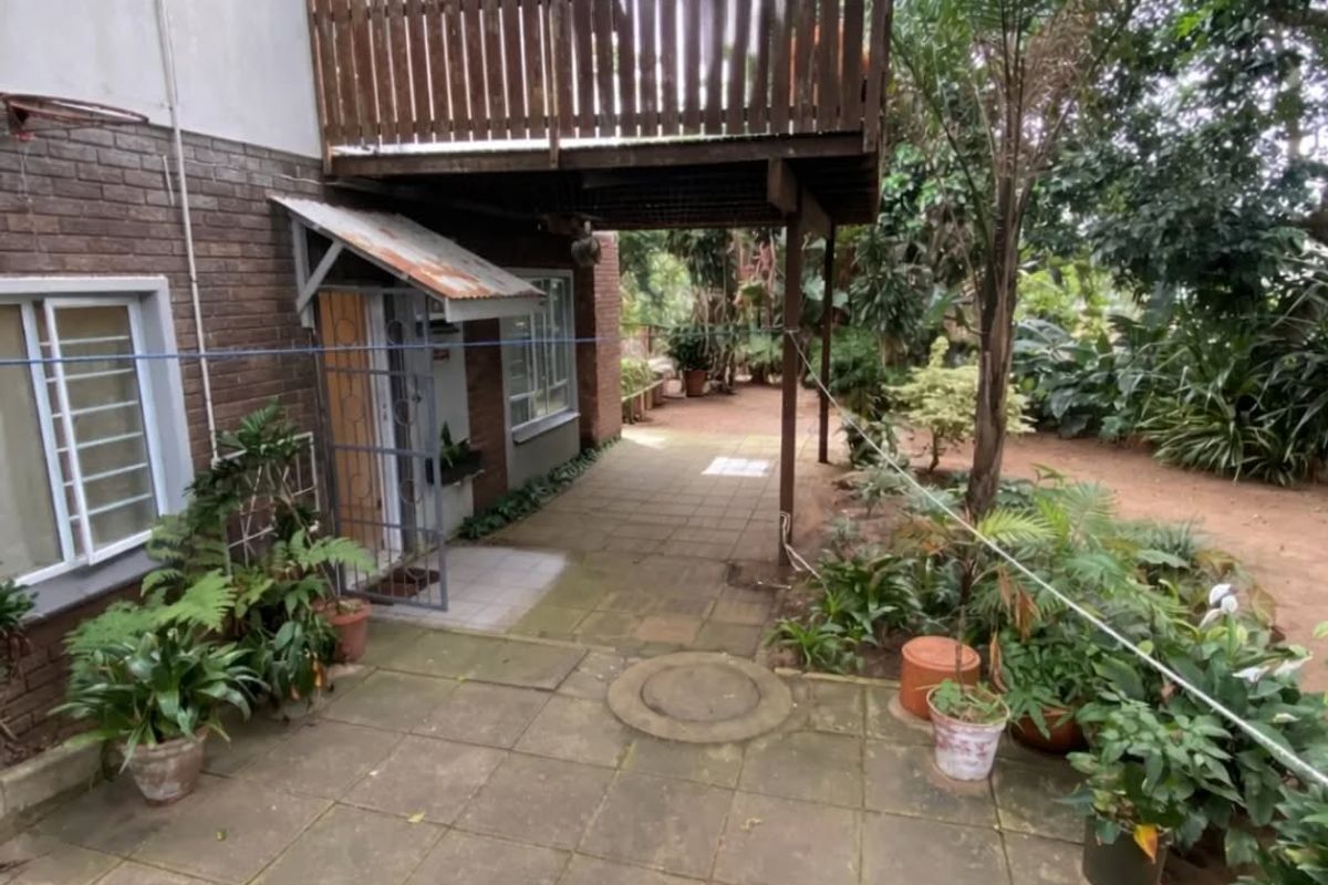 Rear exterior view featuring a paved patio area, a wooden balcony structure, and a brick facade with a metal-covered entrance.