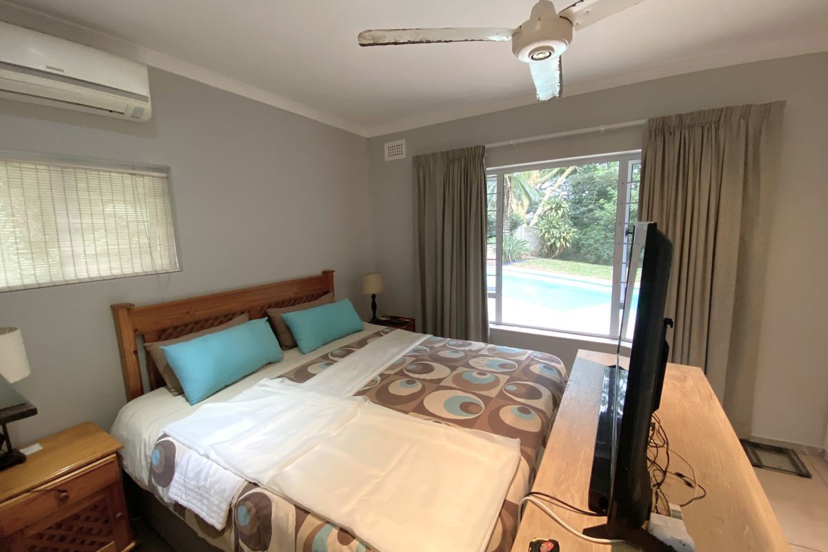A bedroom featuring a ceiling fan, split-system air conditioning, and a window view overlooking the pool area.