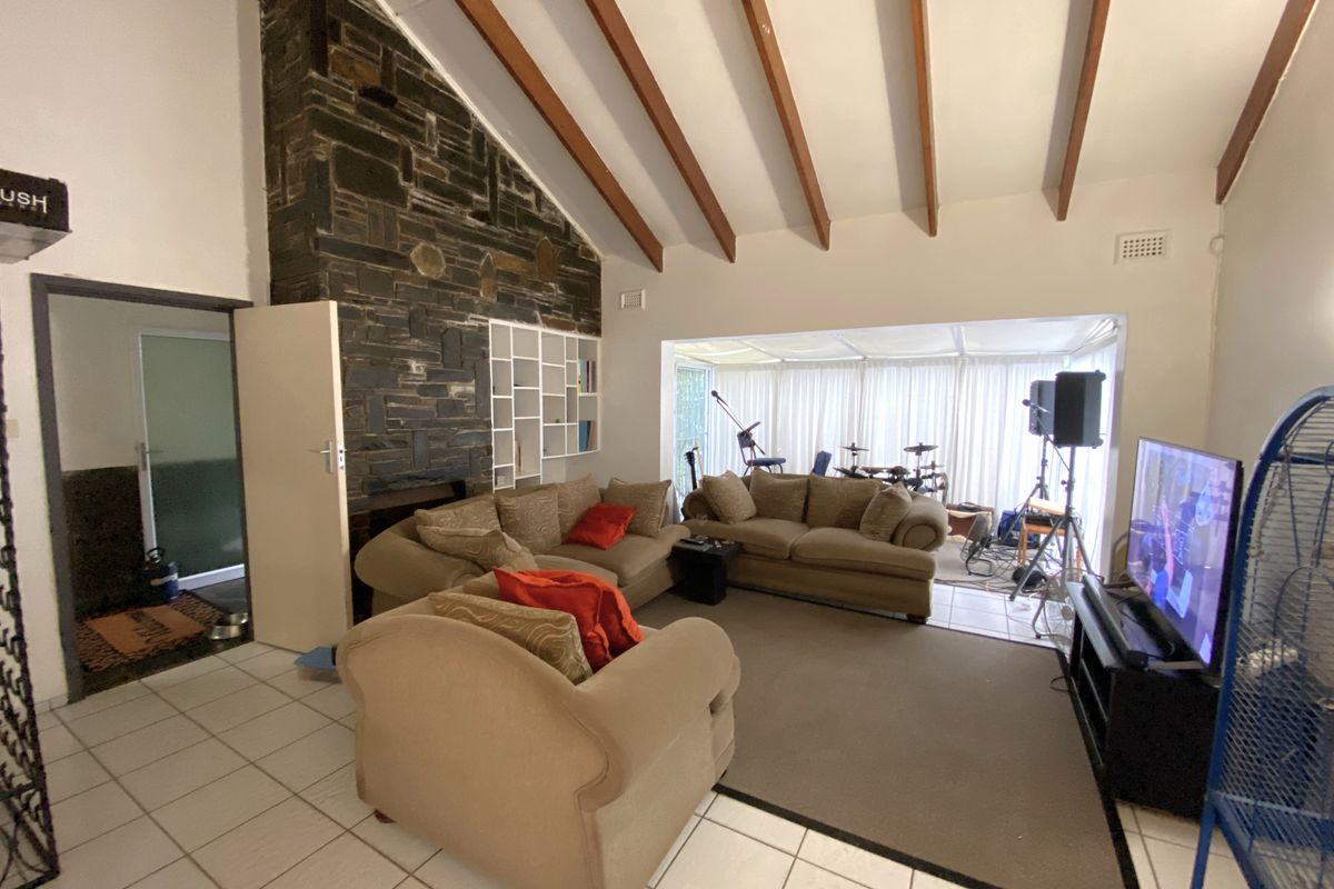 Spacious living room featuring a striking stone fireplace, vaulted ceilings with exposed timber beams, and tiled flooring throughout.