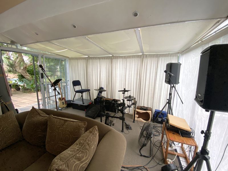 Enclosed patio area featuring sliding glass doors, recessed lighting, and a fabric ceiling shade, currently utilized as a music practice space.