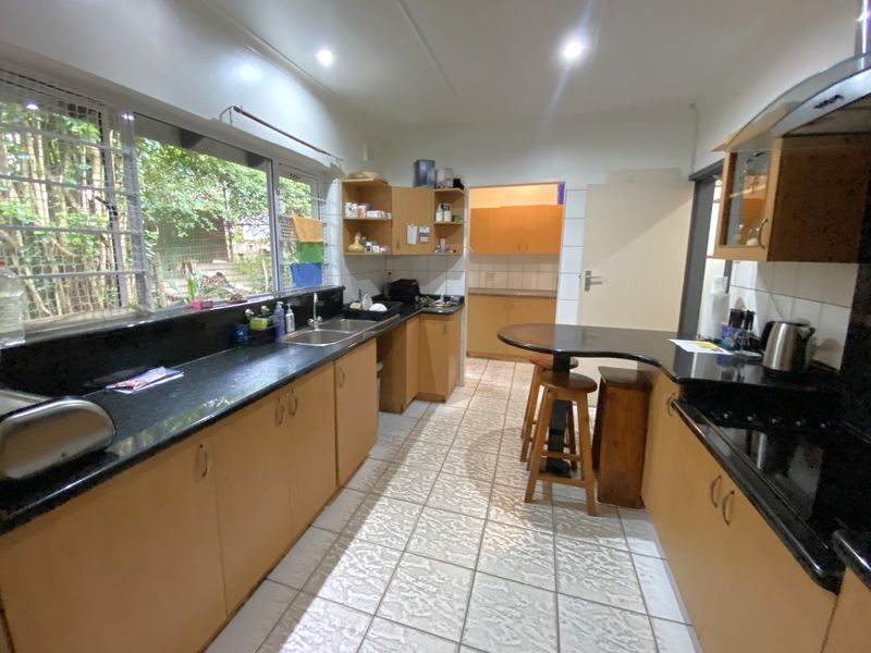 A functional kitchen featuring granite countertops, ample built-in cabinetry, a double basin sink, and a breakfast bar, with direct access to a secondary prep area.