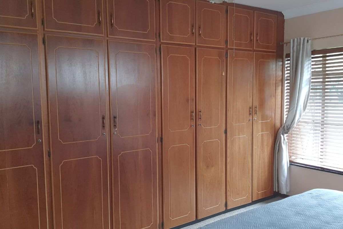 A bedroom featuring extensive floor-to-ceiling built-in wooden cabinetry and window blinds, offering ample storage space.
