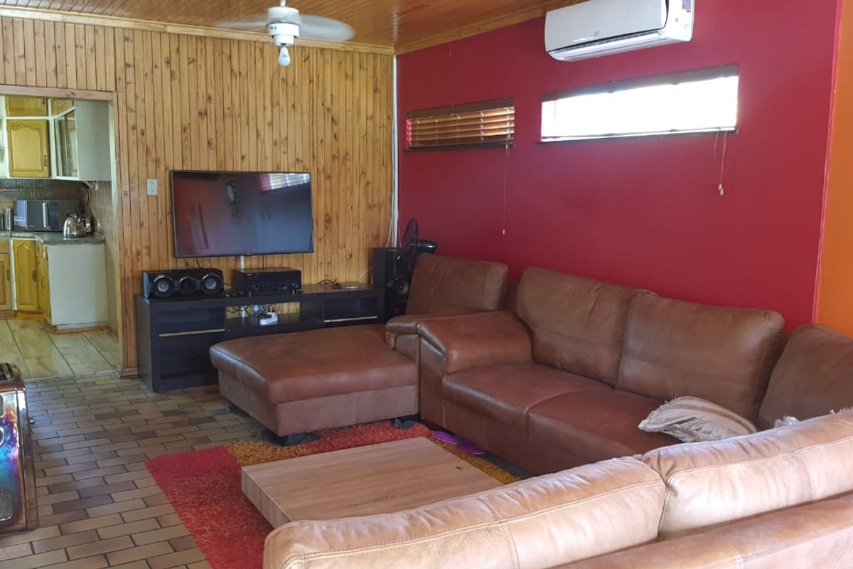 A living room featuring timber wall paneling, tiled flooring, a wood-burning stove, and a split-system air conditioner, with an adjacent view into the kitchen.