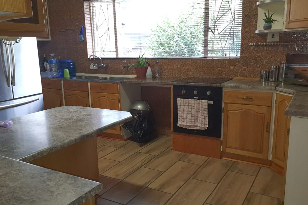 A functional kitchen featuring laminate cabinetry, stone-look countertops, built-in oven, and tiled flooring, offering potential for a modern cosmetic update.