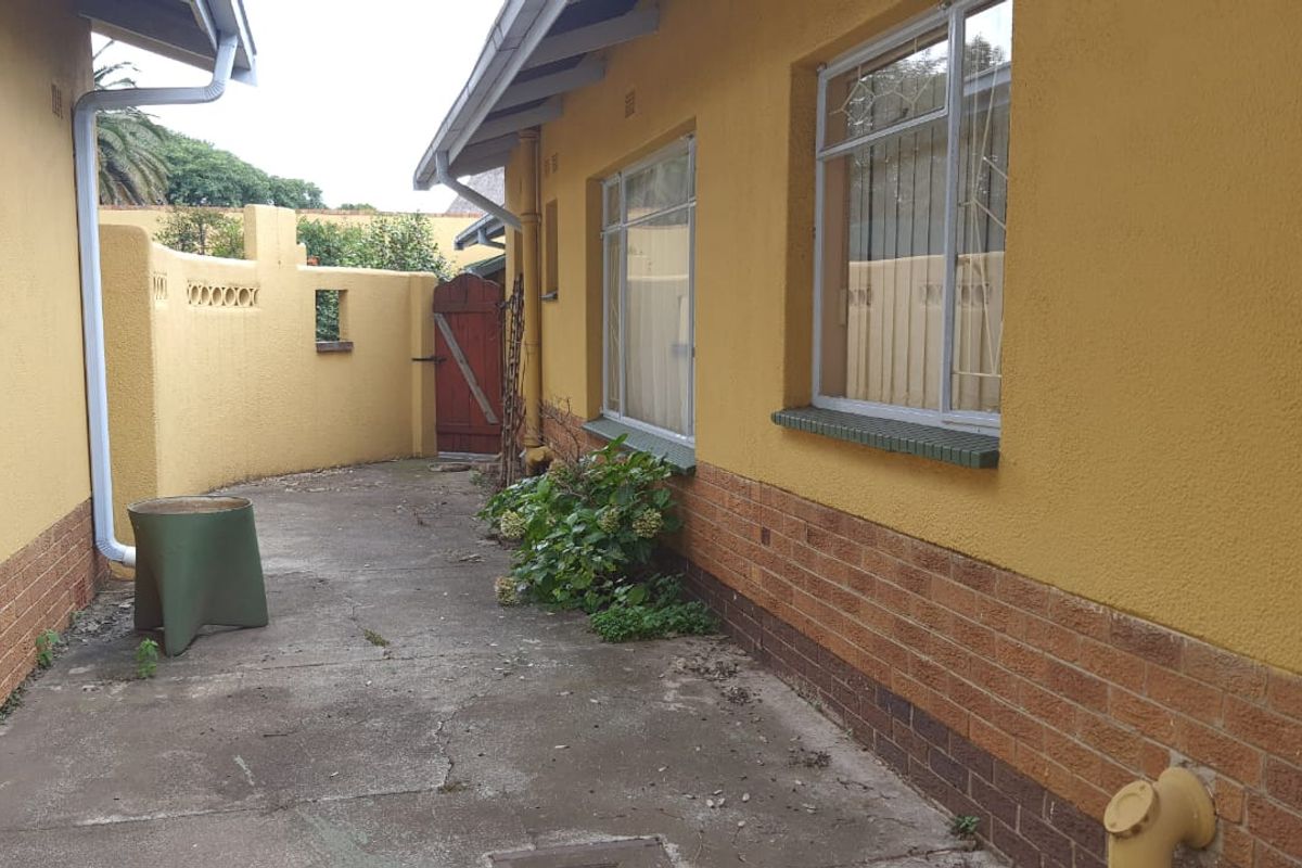 A rear exterior view of the property featuring a concrete paved courtyard, brick boundary wall, and yellow painted exterior walls.