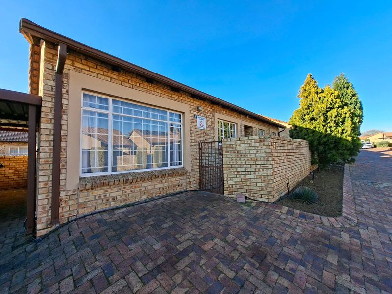 Front elevation of a face brick townhouse featuring a paved driveway, secure gated entrance, and established boundary wall.