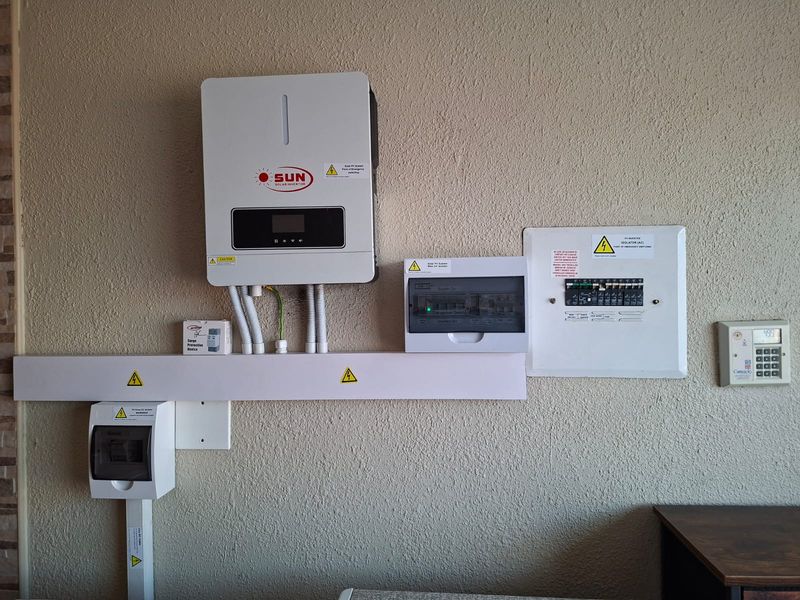 A clean utility wall installation featuring a solar inverter, electrical distribution board, surge protection, and security alarm keypad.