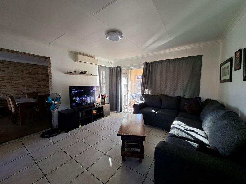 A living room featuring tiled flooring, a wall-mounted air conditioning unit, and a sliding glass door providing access to the outdoor area.