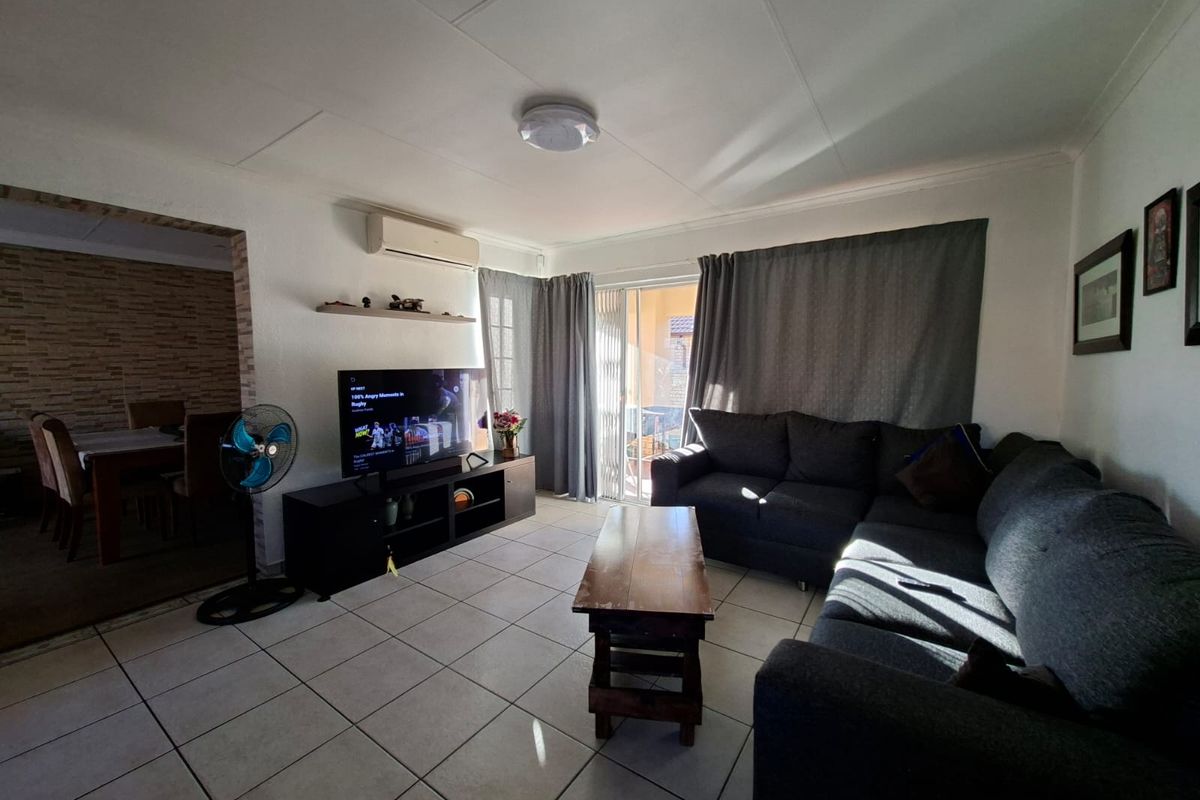 A living room featuring tiled flooring, a wall-mounted air conditioning unit, and a sliding glass door providing access to the outdoor area.