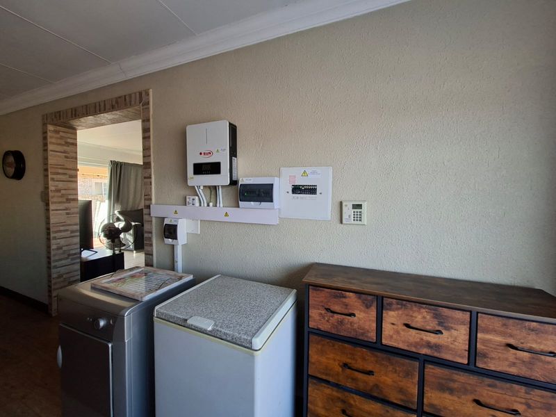 Utility area featuring a wall-mounted solar inverter, electrical distribution board, and alarm system keypad.