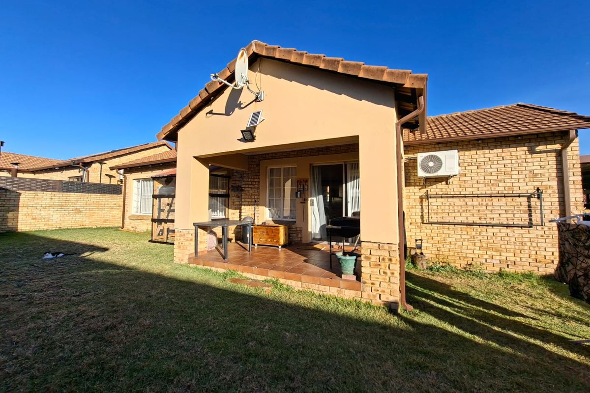 Rear view of the townhouse featuring a covered tiled patio, brick exterior walls, and a private garden area with boundary walling.