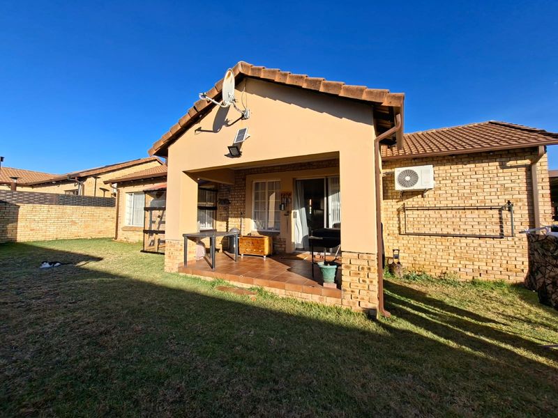 Rear view of the townhouse featuring a covered tiled patio, brick exterior walls, and a private garden area with boundary walling.