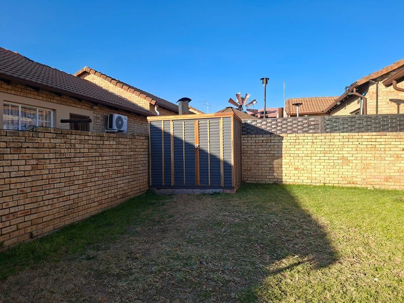 A private rear garden area featuring a brick boundary wall, a metal storage shed, and a small lawn.