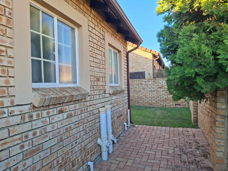 A view of the rear exterior of the townhouse, featuring face brick walls, paved pathways, and established garden boundaries.