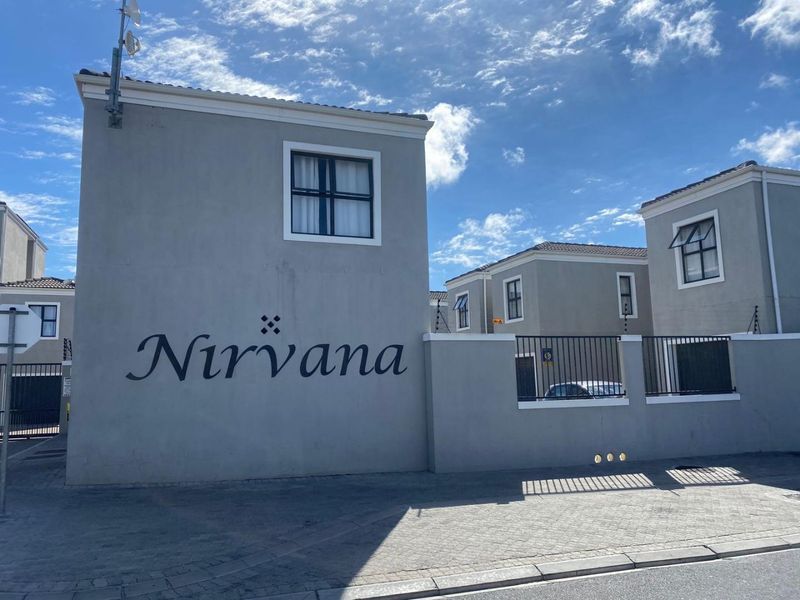 Front exterior view of the Nirvana townhouse complex featuring grey rendered facades, tiled roofing, and secure perimeter fencing with electric security wires.