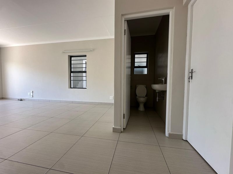 An open-plan living area featuring neutral tiled flooring and a small adjacent bathroom with a toilet and wall-mounted basin.