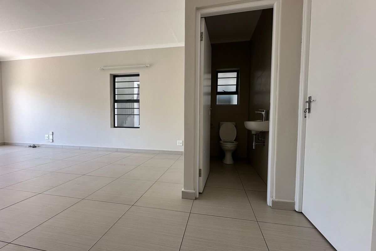 An open-plan living area featuring neutral tiled flooring and a small adjacent bathroom with a toilet and wall-mounted basin.