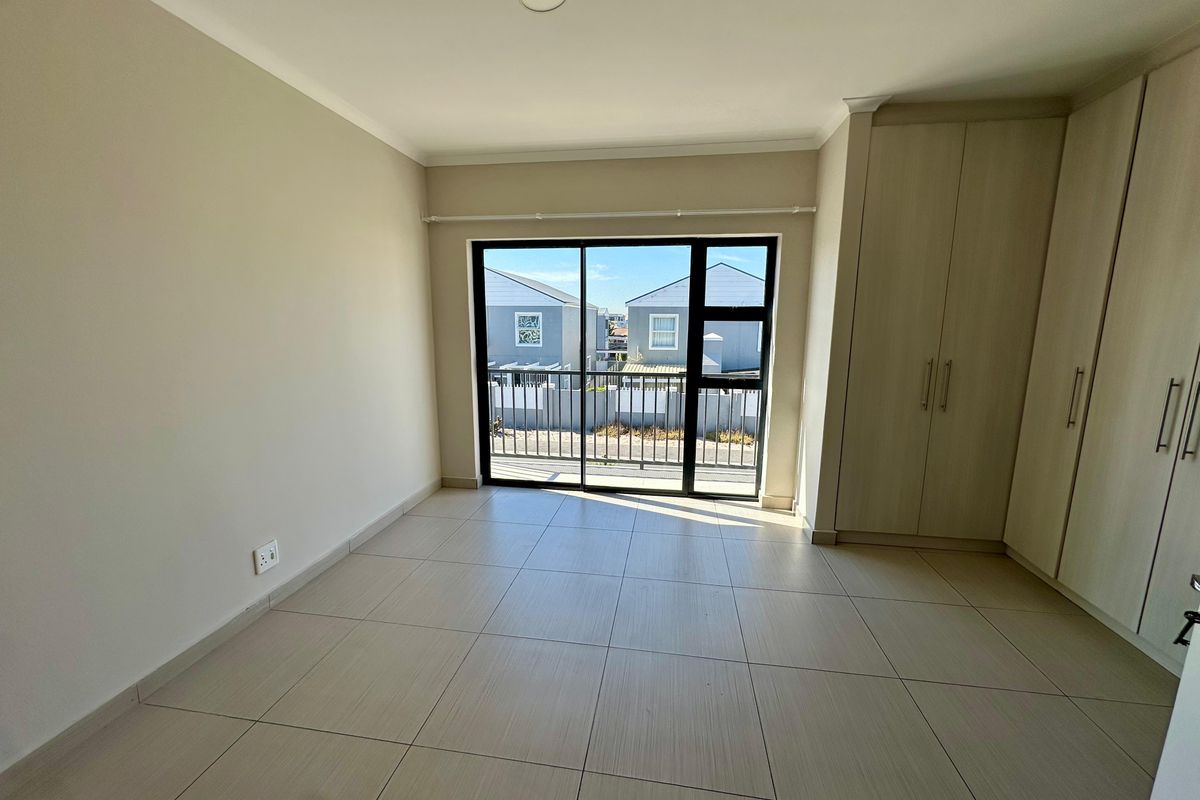 A bright, empty bedroom featuring neutral tiled flooring, built-in cupboards, and a sliding glass door leading to a small balcony.