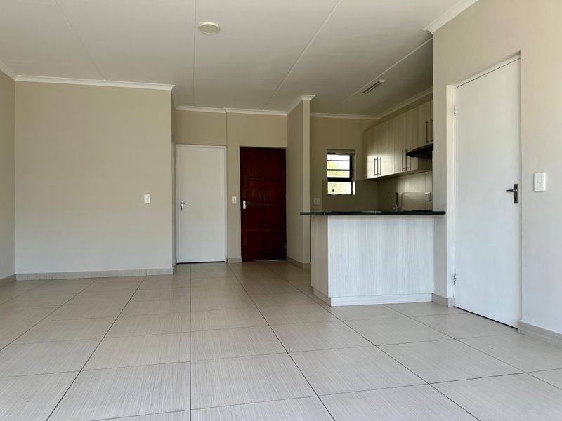 An open-plan living and kitchen area featuring neutral tiled flooring, modern cabinetry, and a breakfast counter in a clean, vacant space.