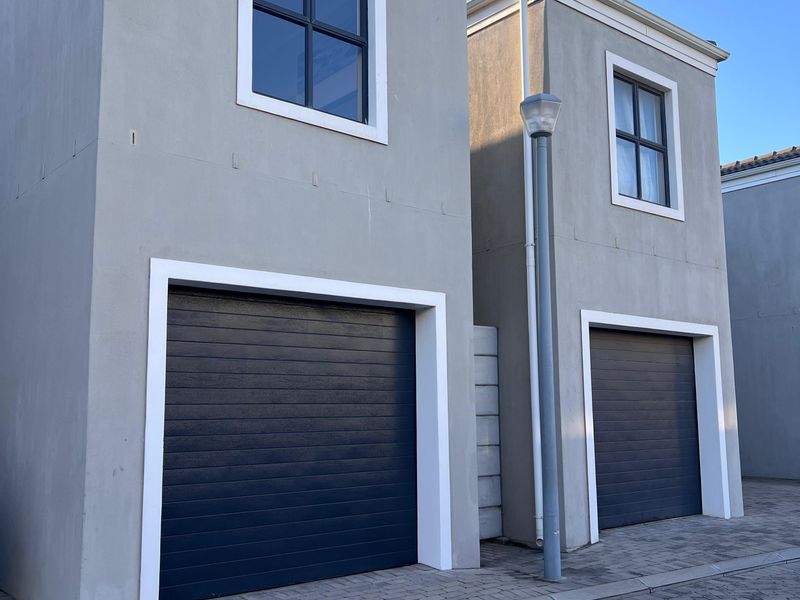 Modern townhouse exterior featuring two dark garage doors, paved driveway, and clean grey facade finishes.